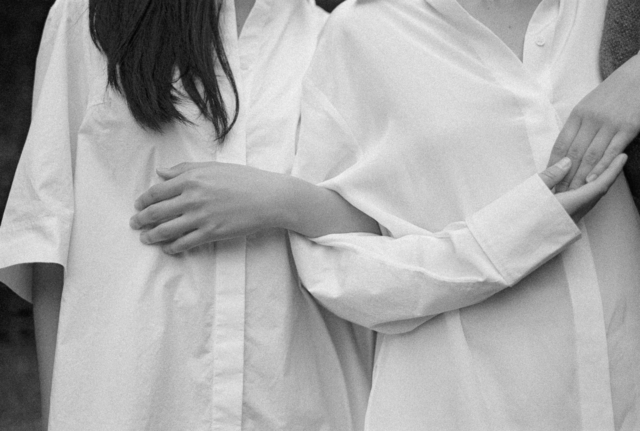 A black-and-white photo showing two individuals wearing white shirts, linking their arms in a close and supportive gesture.